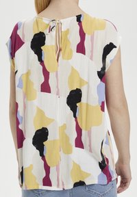Blusa de tejido ligero con estampado floral. Presenta formas abstractas en púrpura, amarillo y negro. Se ata en la parte posterior, tiene mangas cortas y un escote redondo.