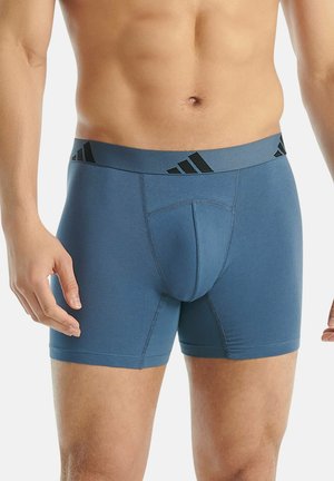 Boxers bleus en tissu lisse avec une ceinture élastique noire ornée du logo Adidas et un design structuré de la poche avant.