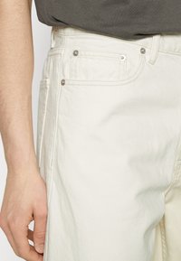 White denim pants featuring a classic five-pocket design, slightly visible stitching, and metal hardware. Soft, textured fabric, slim fit.