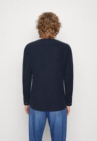 Camicia a maniche lunghe navy con orlo arrotondato, polsini abbottonati e dettaglio sul retro. Realizzata in un tessuto liscio con una leggera lucentezza.