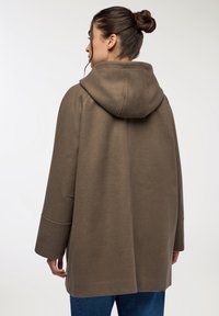 Cappotto marrone con cappuccio, dalla vestibilità rilassata, tessuto morbido e dettagli cuciti, con maniche lunghe e orlo dritto.