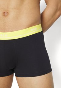 Black boxer shorts with a snug fit, featuring a bright yellow waistband displaying the brand "BOSS" and a subtle white stripe.