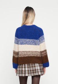Strickpullover mit horizontalen Streifen in Blau, Creme, Braun und Grau. Lockere Passform, runder Ausschnitt und weiche Textur, kombiniert mit einem karierten Rock.