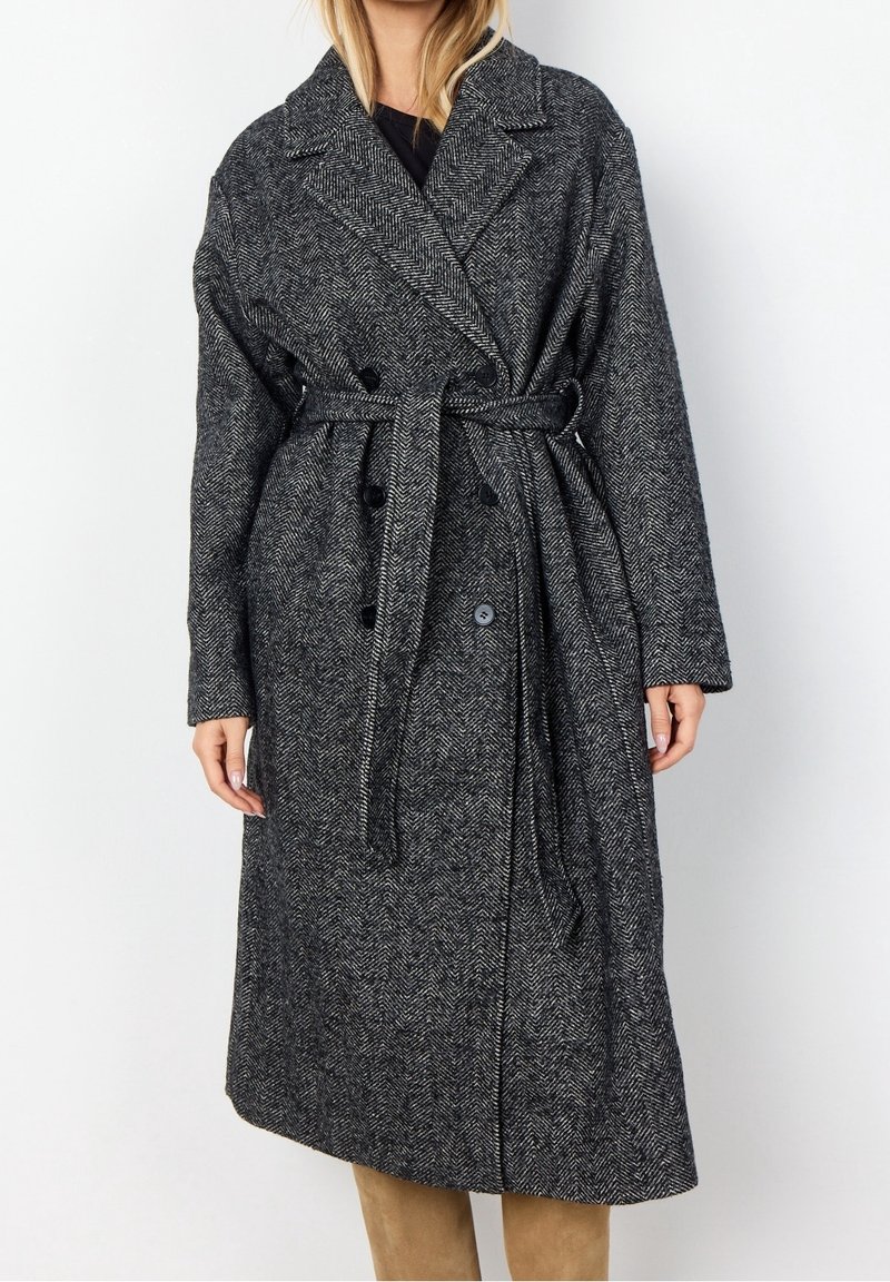 Czarny i szary płaszcz w jodełkę z wełny z paskiem, podwójnym zapięciem, szerokimi klapami i bocznymi kieszeniami, sięgający do połowy łydki.