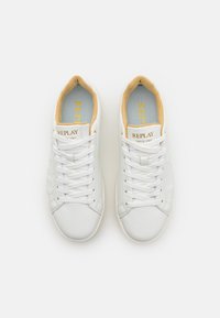 Des baskets blanches en cuir lisse avec un intérieur beige clair. Elles disposent de lacets blancs, d'une semelle plate et du logo "REPLAY" sur la languette.