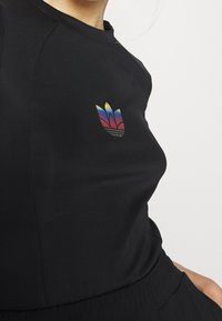 Černý sportovní top s kulatým výstřihem a krátkými rukávy. Obsahuje vícebarevné logo připomínající tři okvětní lístky na levé části hrudníku.