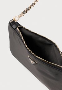 Μαύρο τσαντάκι χειρός από νάιλον με χρυστό φερμουάρ, διακοσμημένο με τριγωνικό λογότυπο και πλεκτό λουρί αλυσίδας. Το εσωτερικό φαίνεται ευρύχωρο και επενδεδυμένο.