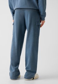 Wyblakłe niebieskie spodnie dresowe o luźnym kroju z bocznymi kieszeniami, prążkowanym paskiem w talii i miękką fakturą materiału. Lekko zwężane u dołu nogawki.