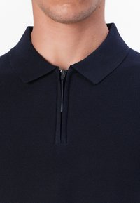 Marineblå polo med glidelås på kragen, laget av teksturert stoff, med korte ermer og en tettsittende design. Enkel og moderne i stilen.