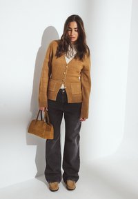 Khaki kardigán s gombíkmi a prednými vreckami, nosený cez smotanový top. Kombinovaný s tmavými džínsami a malou hnedou semišovou kabelkou.