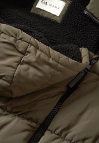 Zielona ocieplana kurtka z czarną podszewką z polaru i czarnym zamkiem błyskawicznym; widoczny kołnierz oraz fragment metki „C&A MAMA” wewnątrz kurtki.