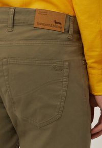 Pantalones caqui con una tela texturizada, que presentan un parche de cuero etiquetado "harmont&blaine" y una sutil silueta de perro. Diseño del bolsillo trasero incluido.