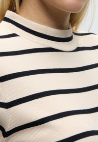 Κοντινό πλάνο ενός ατόμου που φοράει εκρού ριμπ πλεκτό πουλόβερ με μαύρες οριζόντιες ρίγες και στρογγυλή λαιμόκοψη.