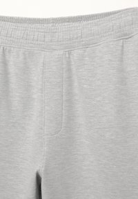 Pantalon gris clair avec taille élastique, braguette à l'avant et tissu doux et lisse au toucher.