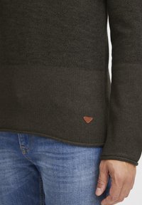 Dark green knitted sweater with a textured pattern, rounded hem, and a small brown leather label featuring "Belended 1992" on the bottom.