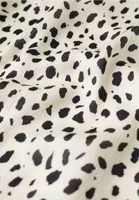 Tissu à motifs noir et blanc présentant une texture lisse avec des taches noires de tailles variées sur un fond crème clair.