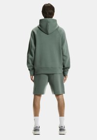 Hoodie en bijpassende shorts in gedempt groen, gemaakt van zacht materiaal. Bevat een kangoeroezak en een logoaccent op de shorts.