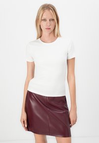 Vit räfflad kortärmad topp som bärs tillsammans med en burgundyfärgad faux leather kjol. Kjolen har en slät yta och en minimal design.