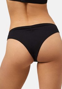 Braga negra de algodón con textura suave, con un borde con borde ondulado a lo largo de la cintura y un sutil detalle fruncido en la parte trasera.