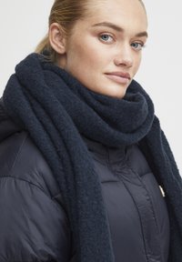 Dark blue, oversized scarf made of soft, textured fabric wrapped around the neck, paired with a shiny black puffer jacket.