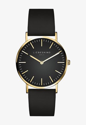 Rund sort ur med gyldne detaljer, der har et minimalistisk design, enkle timemarkører og et blødt sort gummirem.