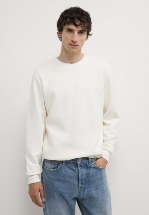 White textured sweatshirt with a crew neck, long sleeves, and ribbed cuffs, paired with light blue denim jeans, front view.