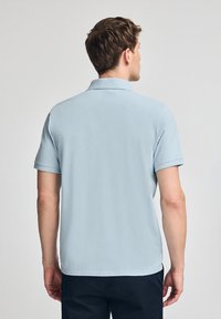Camisa polo azul claro, de manga corta, con cuello clásico, textura suave, de diseño liso y dobladillo recto, combinada con pantalones cortos oscuros.