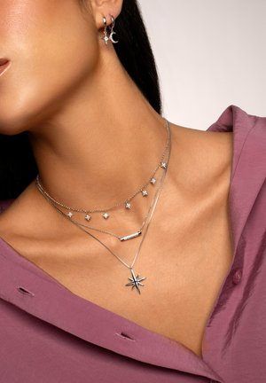 Silbernes Schmuckset mit geschichteten Halsketten, die Stern- und Balken-Anhänger enthalten, sowie passenden Creolen. Die Oberfläche ist poliert und reflektierend.