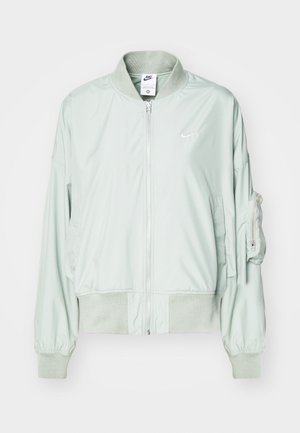 Chaqueta bomber verde claro hecha de una tela suave, con cierre de cremallera en la parte delantera, puños acanalados y un bolsillo de parche en la manga izquierda.