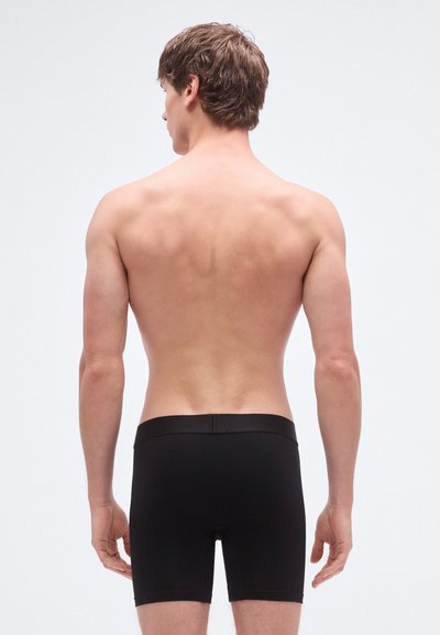 Črne bokser hlače iz gladkega blaga, s prilegajočim se krojem, elastičnim pasom in brez vidnih vzorcev ali poudarkov.
