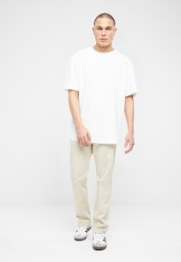 Camiseta de algodón blanca con un corte relajado, combinada con pantalones de un beige claro y zapatillas grises con acentos blancos y tres rayas.