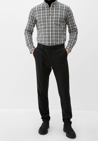 Pantaloni neri da uomo abbinati a una camicia gialla e blu navy a quadri. Presenta un colletto con bottoni e maniche lunghe, con un design slim fit.