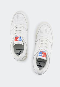 Sneaker bianchi con una tomaia in pelle liscia, punta forata, dettagli grigi e logo colorato sulla linguetta. Design classico con lacci.