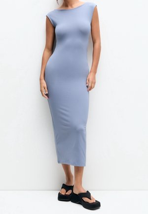 Siddende, ærmeløs, lys blå kjole lavet af glat materiale, der når til midt på læggen. Bæres med sorte platform sandaler med brede stropper.