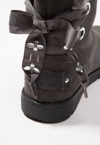 Bota de ante gris oscuro con un lazo de satén, cristales decorativos y acentos de metal plateado en el tacón. Suela texturizada y duradera.