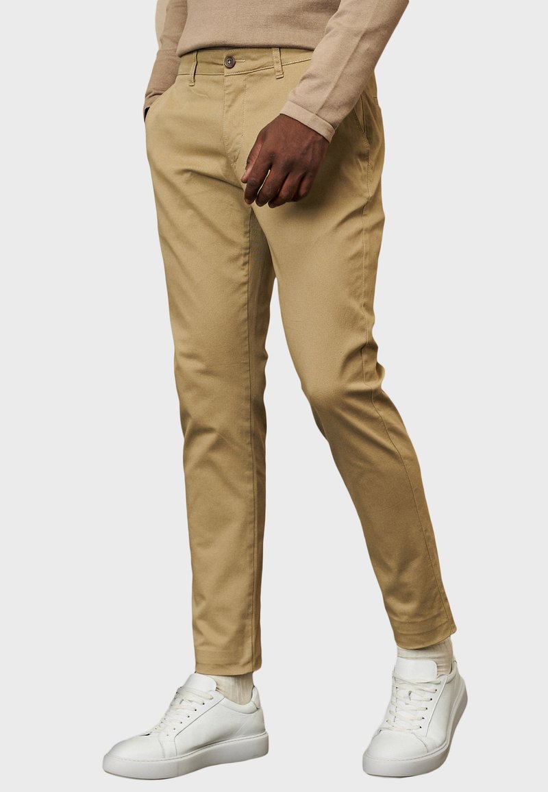 Khaki chinos o slim fit, z zapięciem na guzik, pętelkami na pasek i bocznymi kieszeniami, w połączeniu z białymi skórzanymi sneakersami.
