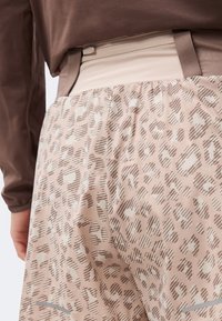 Μπεζ φούστα με καφέ λεοπάρ μοτίβο, ελαστική ζώνη μέσης με φερμουάρ, φορεμένη με μακρυμάνικη καφέ μπλούζα, δείχνοντας την περιοχή της μέσης και των γοφών.