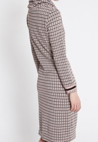 Robe mi-longue en motif pied-de-poule rose et marron, avec un col drapé et des manches longues aux poignets contrastants.