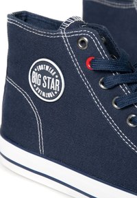 Pantofi sport înalți din pânză bleumarin, cu cusături albe, talpă din cauciuc, ochiuri roșii și un patch circular cu logo-ul "BIG STAR" pe lateral.