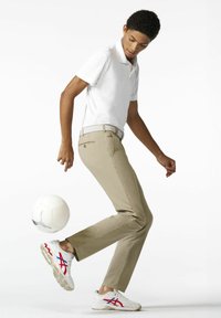 Khaki broek, wit polo shirt en witte sneakers met rode en blauwe accenten; onderwerp voert een truc uit met een voetbal.