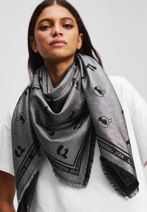 Zilveren sjaal met zwarte accenten en een algehele print. Heeft een driehoekige vorm, franjes aan de randen en een zachte, gestructureerde afwerking.