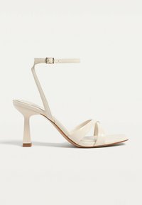 Sandales à talons hauts beige avec un orteil carré, dotées de brides croisées, d'une fine bride de cheville et d'un talon épais avec une légère texture.