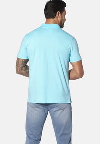 Blaues Polo-Shirt aus Baumwolle, mit kurzen Ärmeln, einem klassischen Kragen und einem geraden Saum. Tragen mit hellen Jeans.