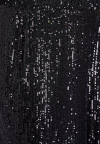 Tela negra adornada con lentejuelas plateadas brillantes esparcidas, creando una superficie texturizada con diferentes reflejos de luz. Se observa un detalle de diseño plisado.