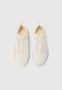 Para skośnych butów Nike w kolorze off-white z zapięciem na sznurowadła, perforowanym wierzchem oraz pętelkami z tyłu na jednolitym białym tle.