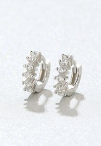 Pendientes de aro de plata con cinco piedras redondas claras, con un acabado pulido y un detalle de cierre visible. Textura suave y brillante.