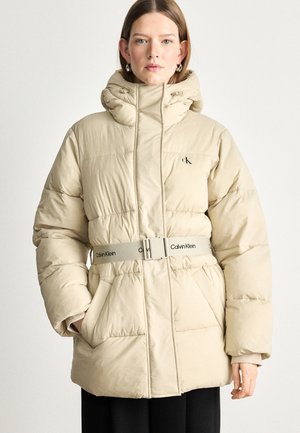 Beige pufferjacka med hög krage, åtdragen midjebälte med "Calvin Klein"-logotyp och synlig sömnad. Två sidofickor ingår.