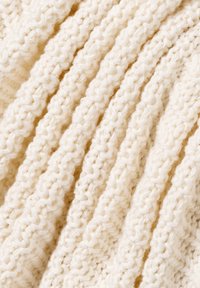 Cremfarbener Strickstoff mit erhabenen, strukturierten Mustern, der dicke, grobe Maschen und ein weiches, plüschiges Aussehen aufweist.