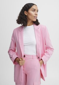Pink tailored blazer with notch lapels, long sleeves, and a relaxed fit, paired with a white fitted T-shirt and matching pink trousers.