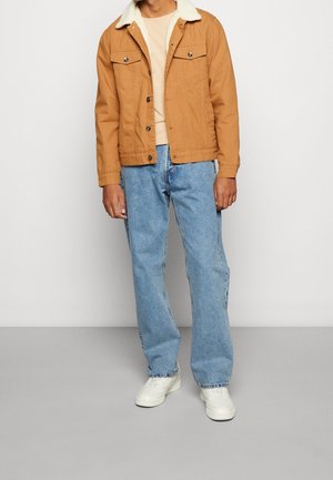 Tanfarvet denimjakke med shearling-krave, to brystlommer, kombineret med lyseblå jeans med lige ben og hvide sneakers.